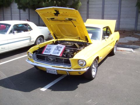 2002 Ford Mustang - A yellow 1967 Ford Mustang is displayed with its hood open, revealing the engine and a book of information.