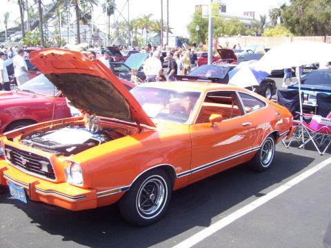 2002 Ford Mustang - An orange 1975 Ford Mustang II is displayed with its hood up at a car show.