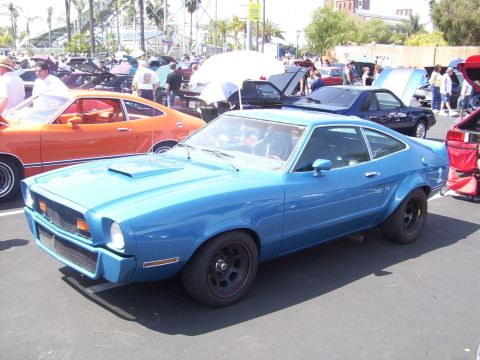 2002 Ford Mustang - A blue 1975 Ford Mustang II is displayed at a car show, parked next to an orange car.