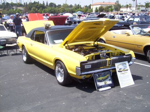 2002 Ford Mustang - A yellow classic car, possibly a Mercury Cougar, is displayed with its hood open at an outdoor car show.