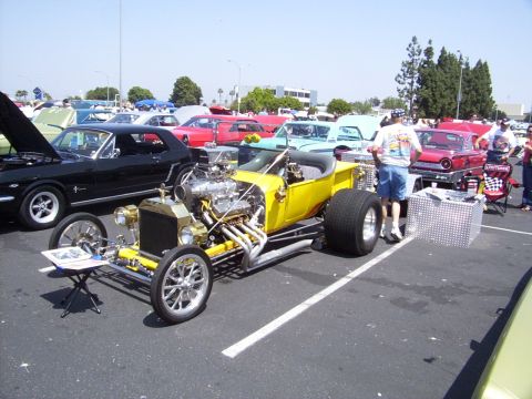 2002 Ford Mustang - A yellow hot rod is displayed at a car show with other vehicles in the background.