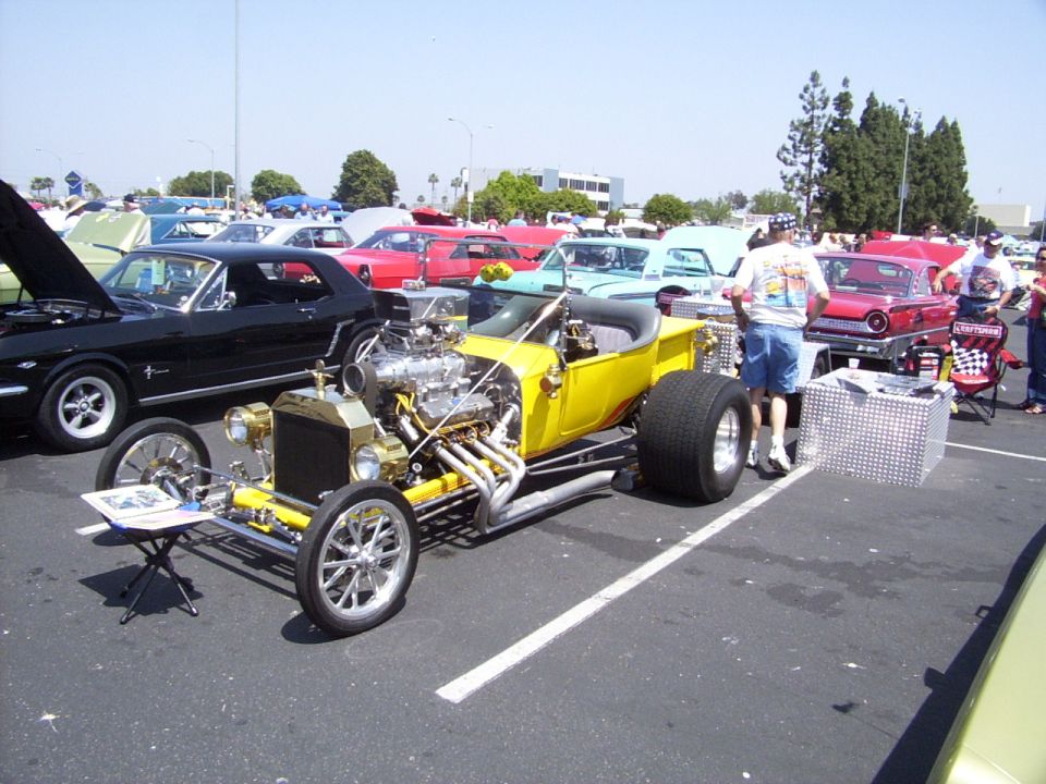 Yellow hot rod with large rear tires, exposed V8 engine, and chrome accents