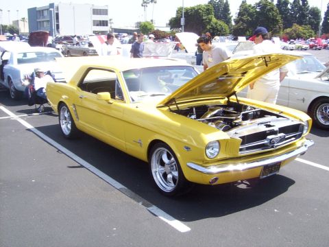 2002 Ford Mustang - A yellow 1965 Ford Mustang is displayed with its hood up at an outdoor car show.