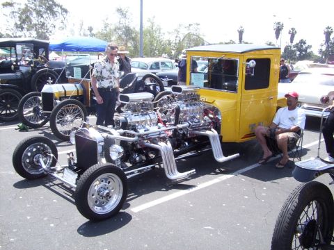 2002 Ford Mustang - A custom yellow hot rod with two powerful V8 engines is displayed at an outdoor event, with other vintage vehicles in the background.