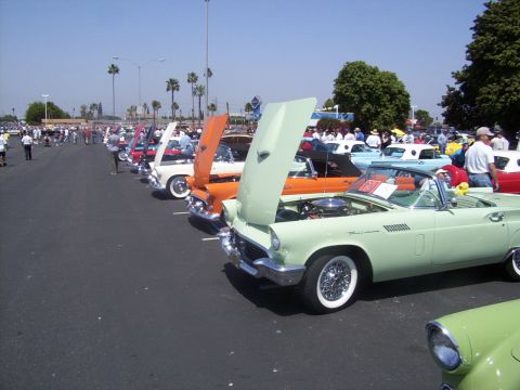 2002 Ford Mustang - A line of vintage cars, mostly convertibles with hoods open, are displayed at an outdoor event on a sunny day.