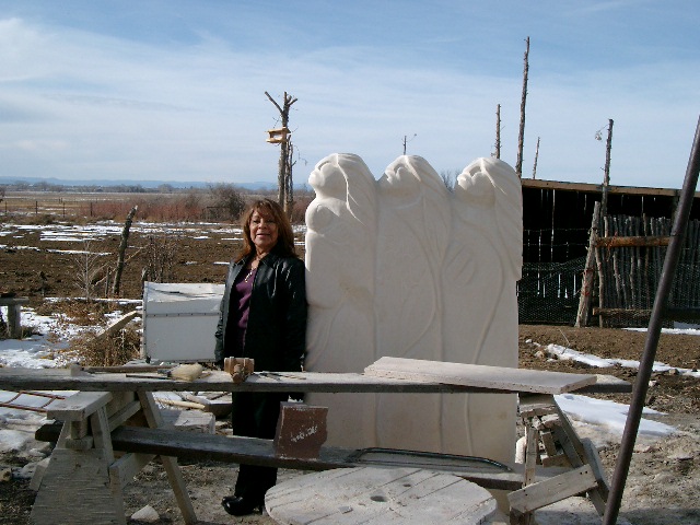 Person standing beside a large white carved stone sculpture in a snowy outdoor work yard