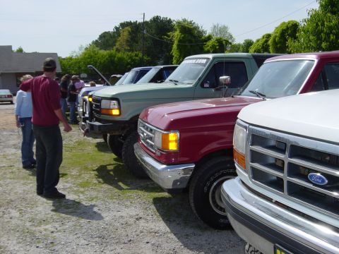 1988 Ford Bronco - Multiple Ford trucks and SUVs are lined up outdoors on a sunny day.