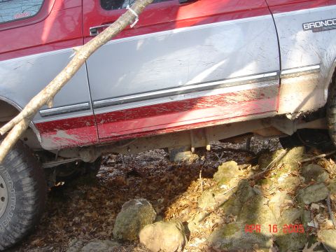 1995 Ford Bronco - A red and silver Ford Bronco is seen from the side, covered in mud and with a branch obscuring the door.
