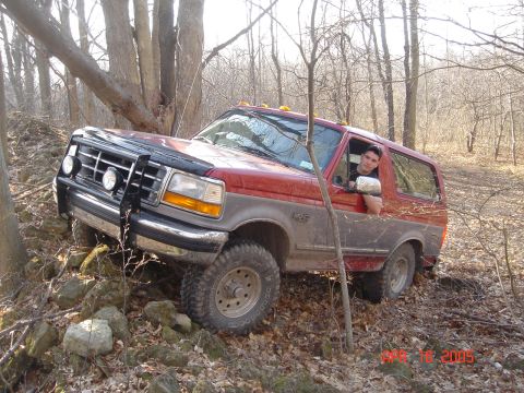 1995 Ford Bronco - The vehicle navigates a rough, wooded path with rocks and fallen leaves on the ground.