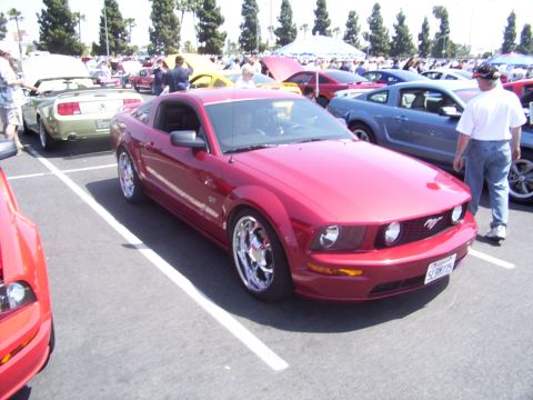 2002 Ford Mustang - A red Ford Mustang is parked at an outdoor car show with other vehicles and attendees.