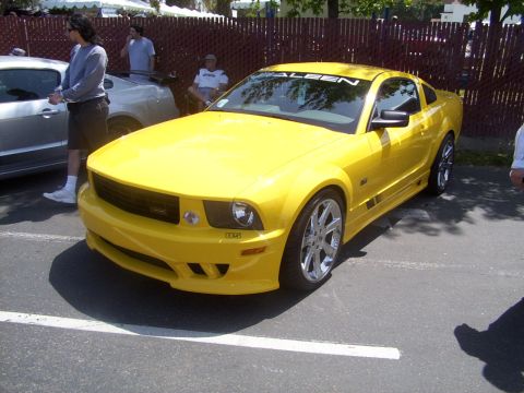 2002 Ford Mustang - A yellow Saleen Mustang is parked next to another car, with people standing nearby.