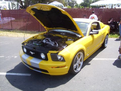 2002 Ford Mustang - Yellow Ford Mustang with hood open, displaying its engine and custom wheels.