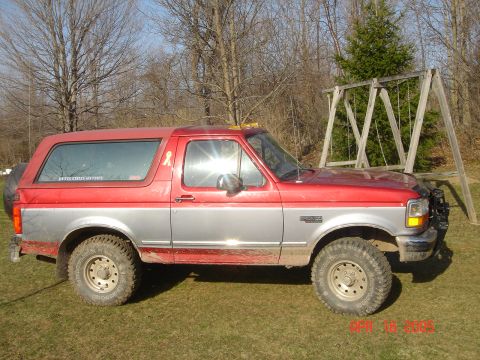 1995 Ford Bronco - A two-tone Ford Bronco is parked on a grassy lawn with a wooden swing set behind it.