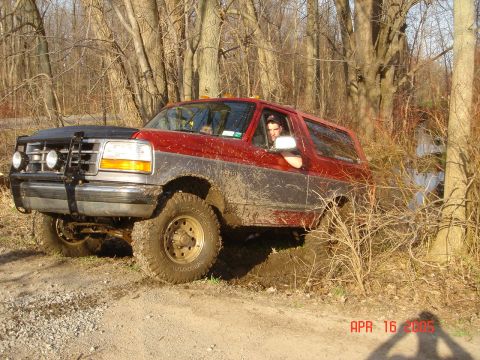 1995 Ford Bronco - A red and silver 1995 Ford Bronco is stuck in the mud while navigating a wooded trail.