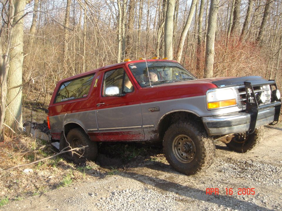 Red and gray 1995 Ford Bronco with aftermarket brush guard, stuck in mud off-road