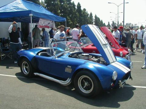 1993 Ford Probe - A blue AC Cobra replica is displayed with its hood open at a car show, alongside other vehicles and attendees.