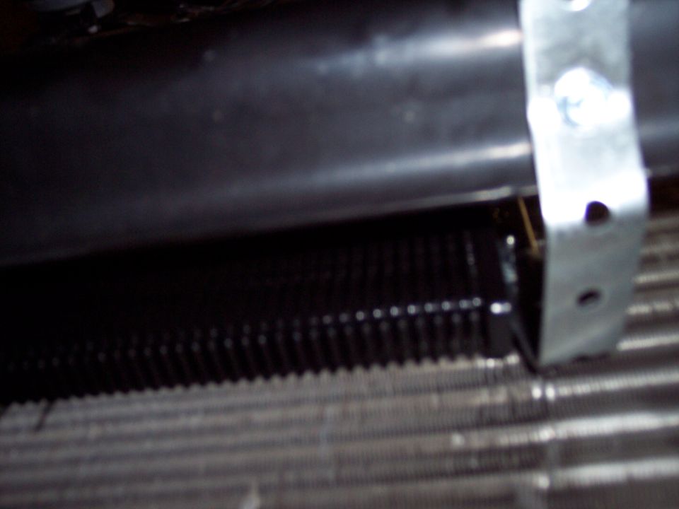 Close-up of black finned cooler mounted against a radiator core with a metal strap bracket