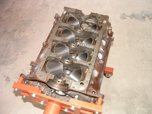 Engine block on an orange stand, showing the cylinder bores and crankshaft bearing saddles