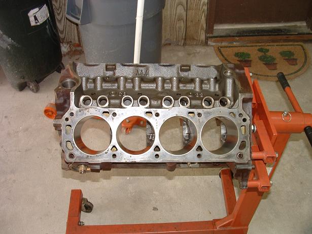 Engine block on an orange engine stand, showing cylinder bores and valve train components
