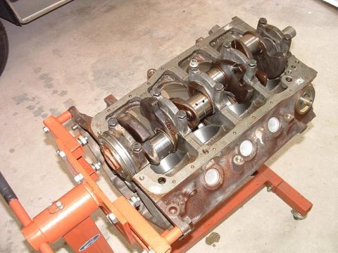 1985 Ford LTD Crown Victoria - The internal components of an engine block are exposed while it is supported by an orange engine stand.