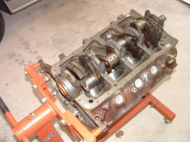 engine block with crankshaft and connecting rods visible, mounted on an orange engine stand