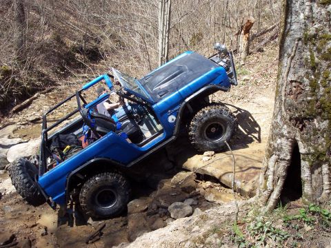 1974 Ford Bronco - A modified blue SUV navigates a challenging rocky terrain on an off-road trail.