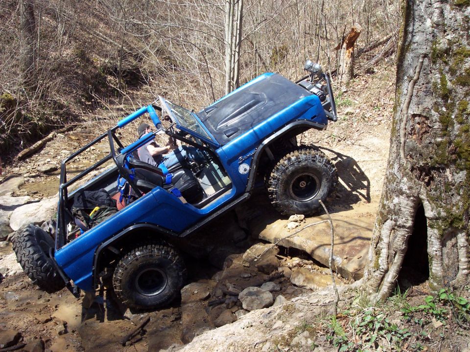 Blue SUV with roll cage climbing over rocks on a trail. Driver visible inside