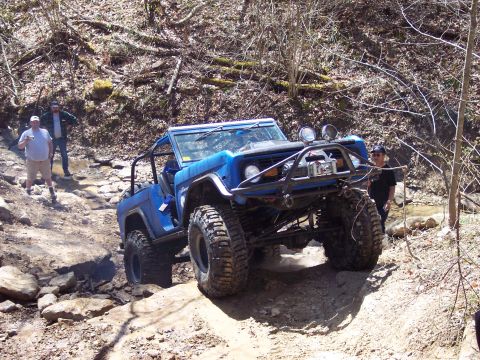 1974 Ford Bronco - A blue 1974 Ford Bronco navigates a challenging off-road course with onlookers present.