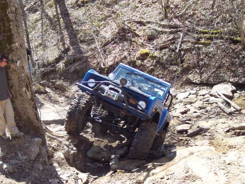 1974 Ford Bronco - Blue 1974 Ford Bronco tackling a challenging off-road course in a wooded area.