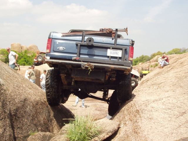 Blue Ford Bronco rock-crawling over granite boulders, rear view, Texas plate
