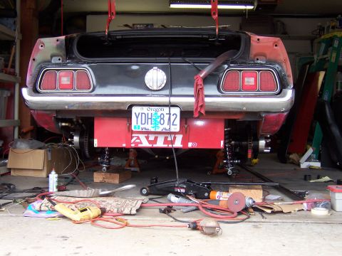 1971 Ford Mustang - Rear view of a 1971 Ford Mustang undergoing maintenance in a garage, with tools and parts scattered around.