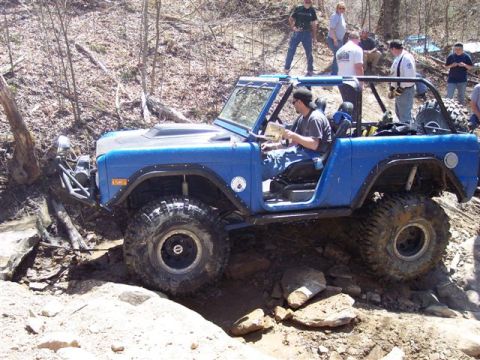 1974 Ford Bronco - A blue 1974 Ford Bronco tackles a challenging off-road course with spectators watching.