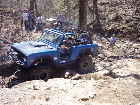 1974 Ford Bronco - A blue 1974 Ford Bronco tackles a challenging off-road course with spectators watching.