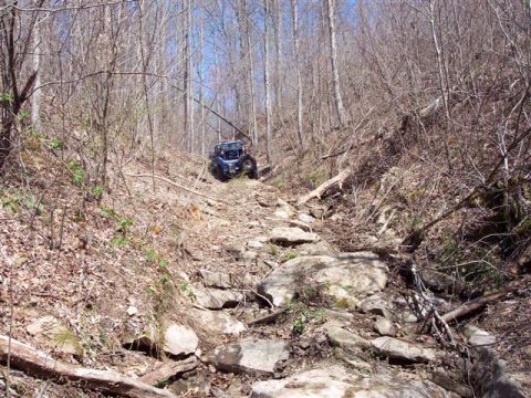 1974 Ford Bronco - UTV tackling a challenging rocky path in a forest during daytime.