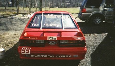 1993 Ford Mustang - A red 1993 Ford Mustang Cobra race car is parked outdoors next to another vehicle.