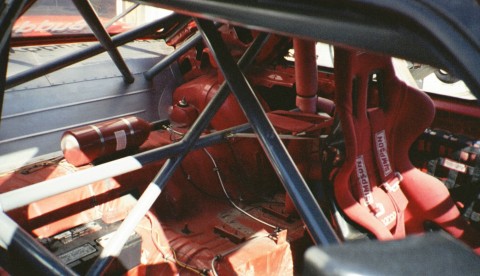 1993 Ford Mustang - The interior of a race car features red Simpson racing seats and a prominent roll cage structure.