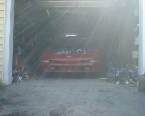 1994 Ford Probe - A red car sits in a garage with its hood open, surrounded by clutter.