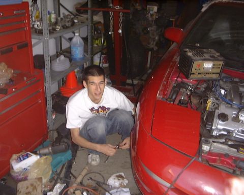 1994 Ford Probe - A man works on a red car in a garage, with tools and a battery charger visible.