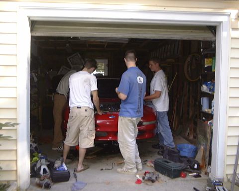 1994 Ford Probe - Several people gather around a red car with its hood open in a cluttered garage.