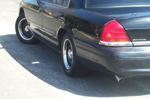 1999 Ford Crown Victoria - The rear of a black sedan is shown, chrome wheels and a visible 'Crown Victoria' badge on the trunk lid.