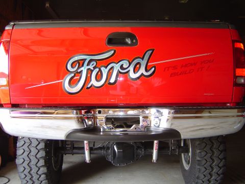 1978 Ford Bronco - The tailgate of a red Ford pickup truck features custom lettering and a chrome bumper.