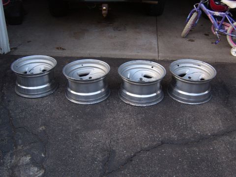 1993 Ford Bronco - Four aluminum alloy wheels are displayed on a cracked asphalt surface, with a bicycle visible in the background.