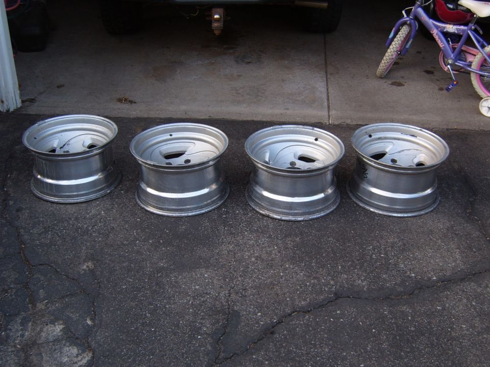 Four silver aluminum alloy wheels with five lug holes and a multi-spoke design, resting on asphalt