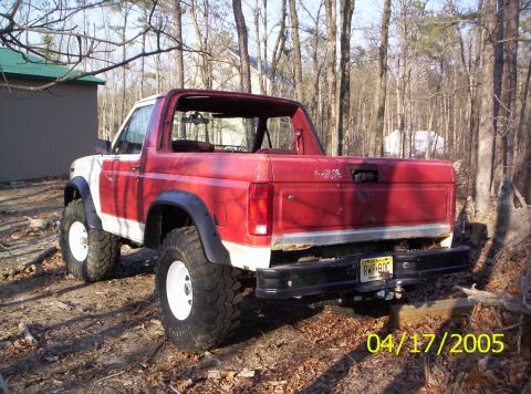 1985 Ford Bronco - This is a red and white Ford Bronco, likely from the early 1980s, with large off-road tires.