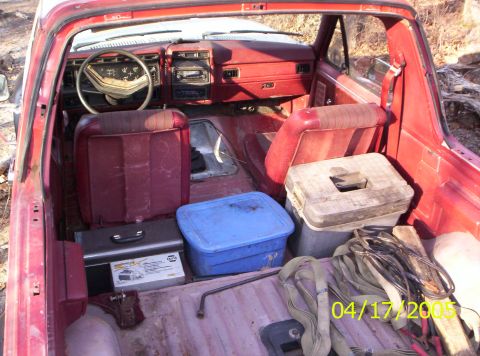 1985 Ford Bronco - The interior of a red pickup truck is shown, filled with various items in the cargo area and on the seats.