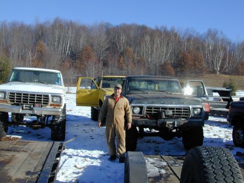 1979 Ford F-150 - A man stands between a white and a black Ford F-150 pickup truck, with a yellow truck behind them.