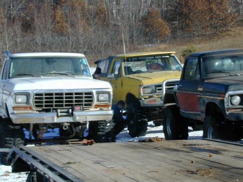 1979 Ford F-150 - Three lifted pickup trucks are parked on a trailer, with the front of a 1979 Ford F-150 prominently displayed.