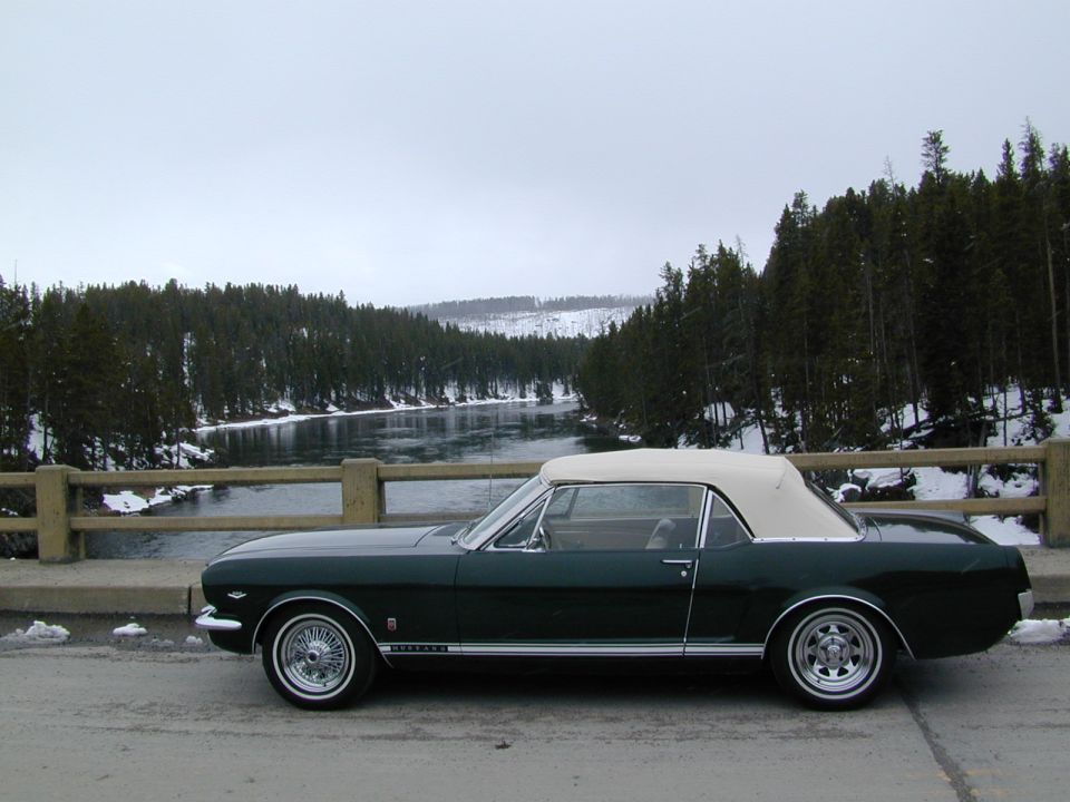 1966 Ford Mustang convertible parked on a bridge with a river and snow-covered trees in the background
