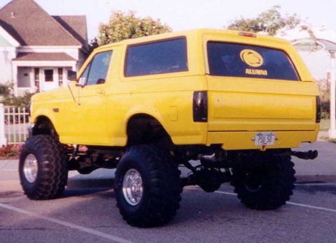 1986 Ford Bronco - A lifted yellow Ford Bronco with large tires is shown from the rear, displaying a PSU Alumni sticker and a custom license plate.