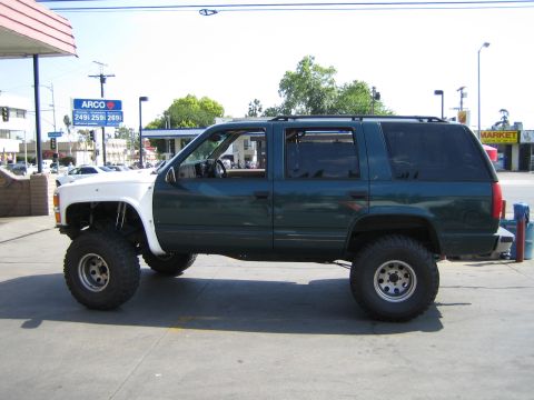 1990 Ford Bronco - lifted green-and-white Chevrolet Tahoe with chrome wheels and mud tires sits in profile at an ARCO gas station.